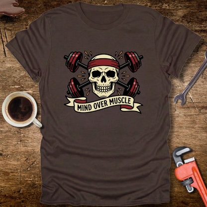 Brown t-shirt with skull and barbell design on a wooden surface with coffee and tools.