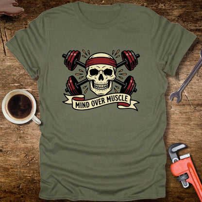 Green t-shirt with skull and barbell design on a wooden surface with coffee and tools.