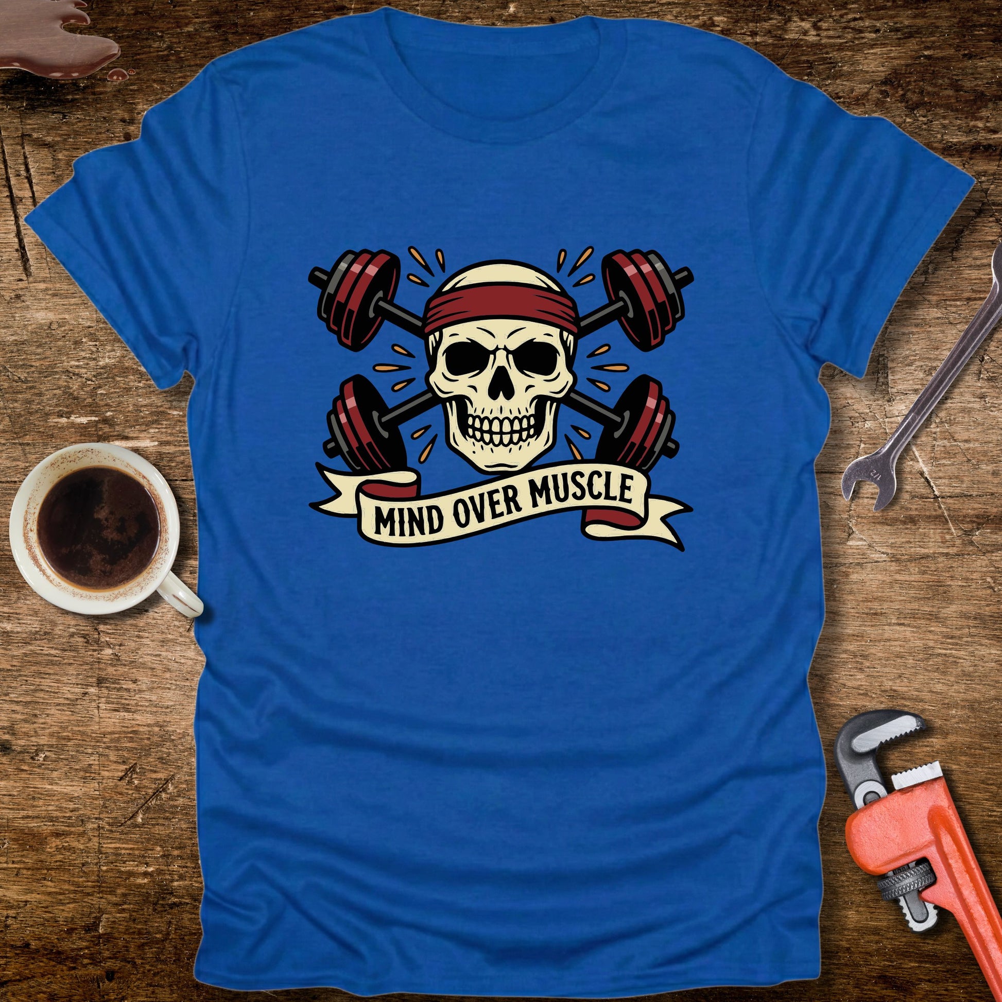 Blue t-shirt with skull and barbell design on a wooden surface with tools and a cup.