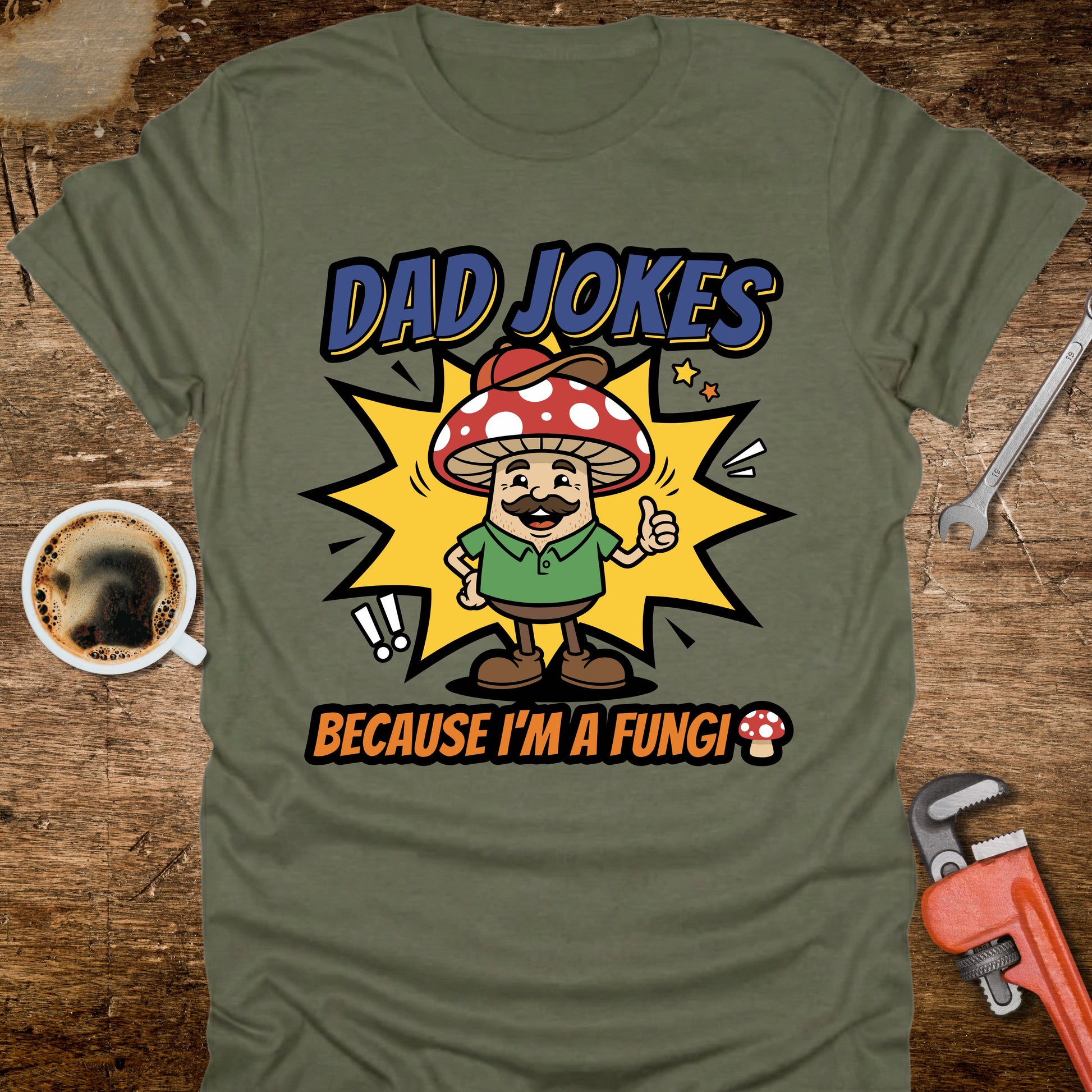 Green t-shirt with a cartoon mushroom character and text on a wooden surface with tools and coffee.