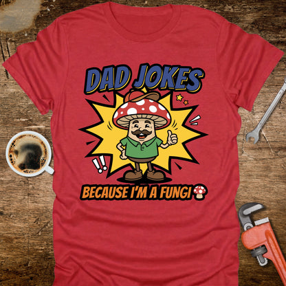 Red t-shirt with a mushroom graphic and text on a wooden surface with coffee and tools.