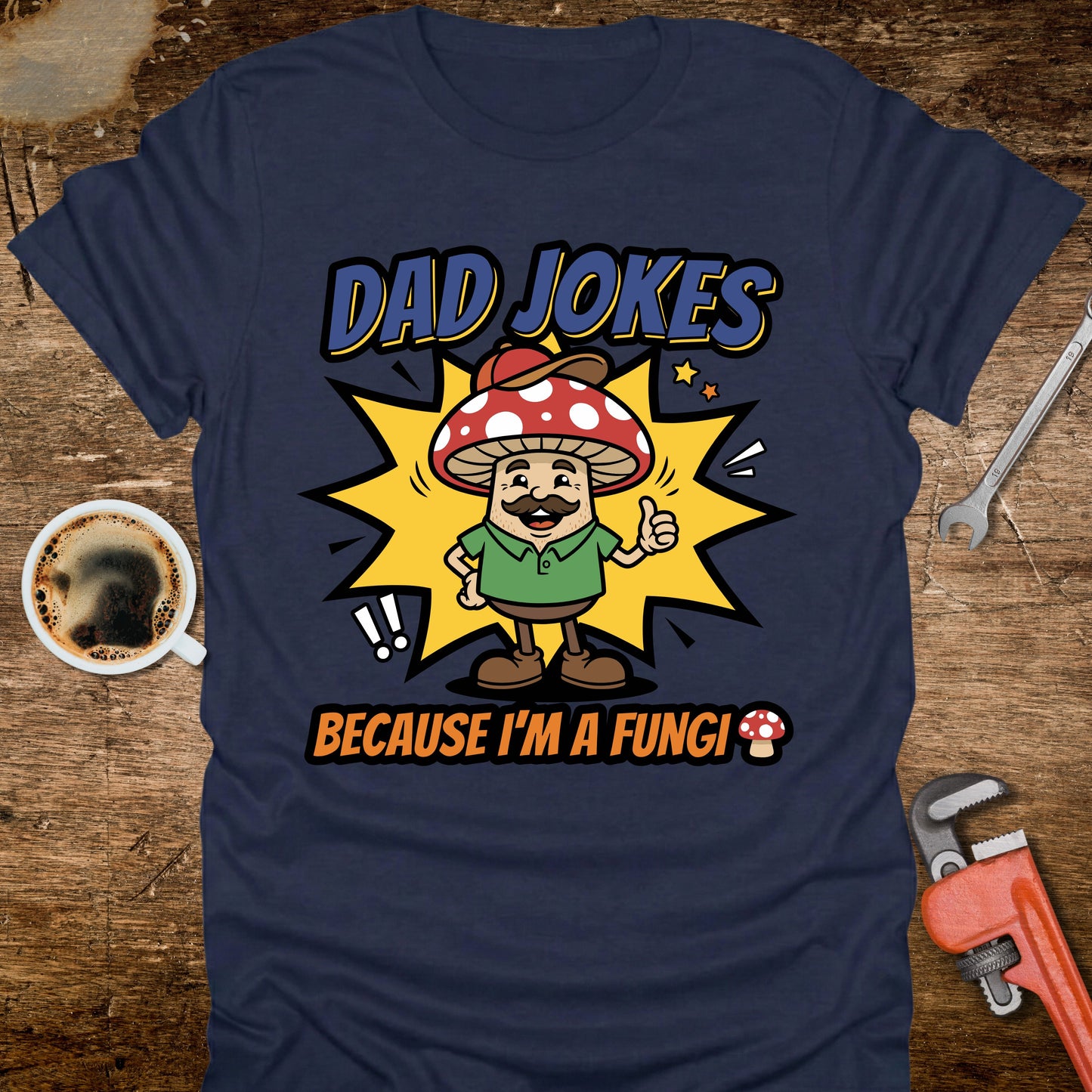 Navy blue t-shirt with a cartoon mushroom character and text on a wooden surface with coffee and tools.