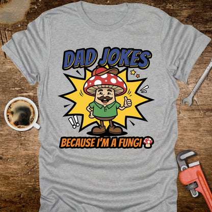 Gray t-shirt with a cartoon mushroom character and text on a wooden surface with coffee and tools.