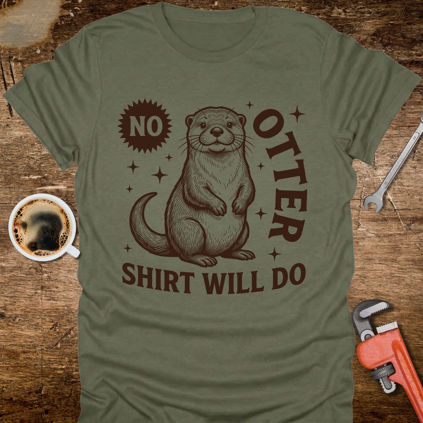 Green t-shirt with an otter graphic and text on a wooden surface with coffee and tools.