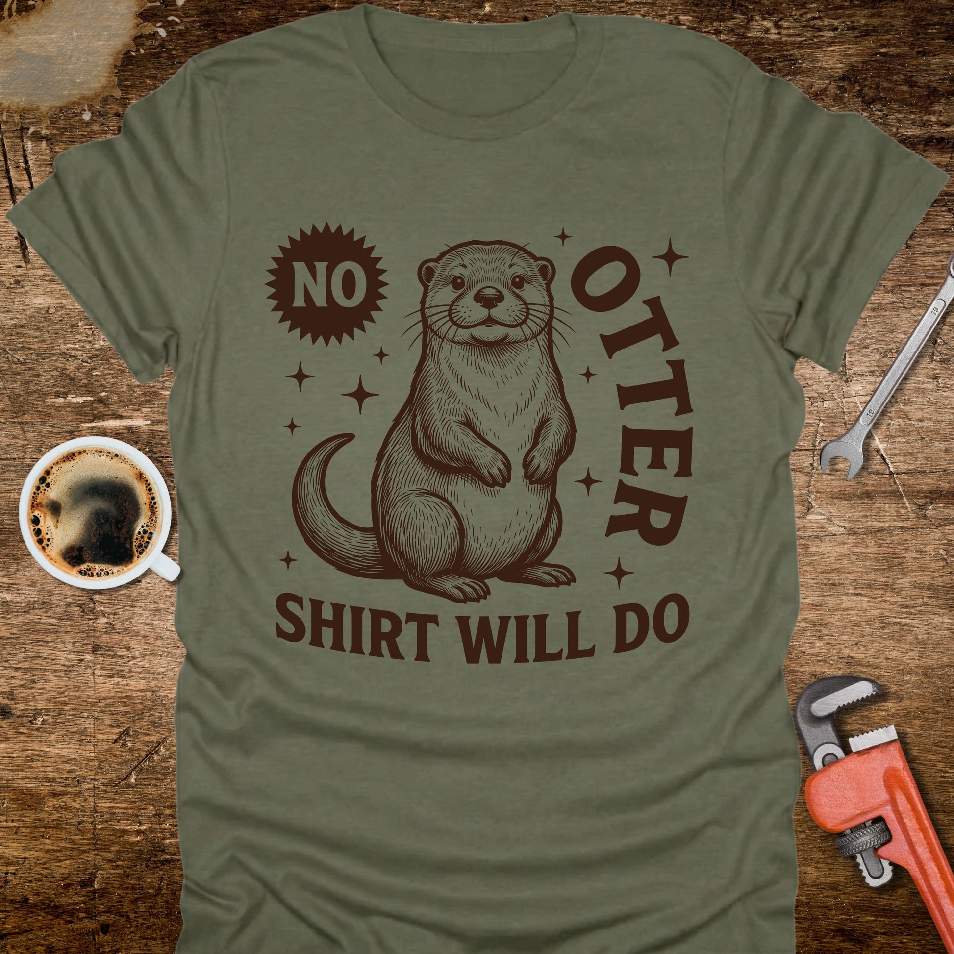 Green t-shirt with an otter graphic and text on a wooden surface with coffee and tools.
