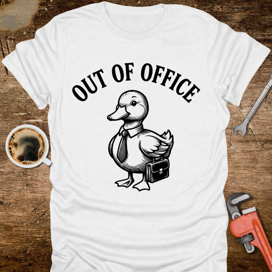 White t-shirt with a duck graphic and 'Out of Office' text on a wooden surface with coffee and tools.