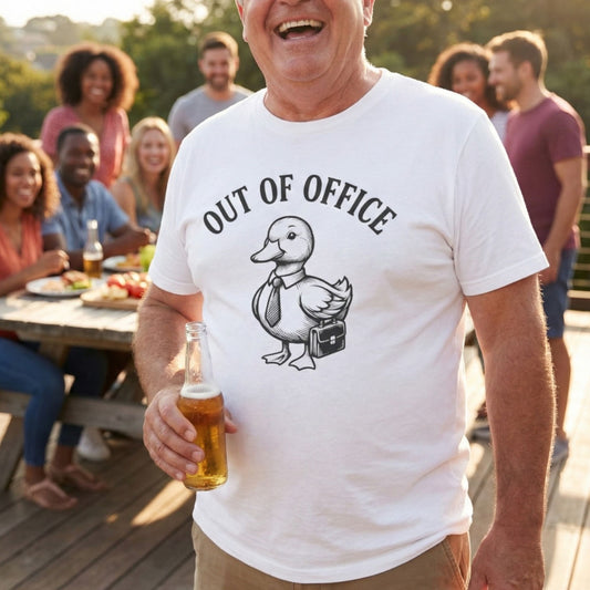 Man wearing a 'Out of Office' t-shirt with a duck graphic, holding a beer, standing outdoors with friends.