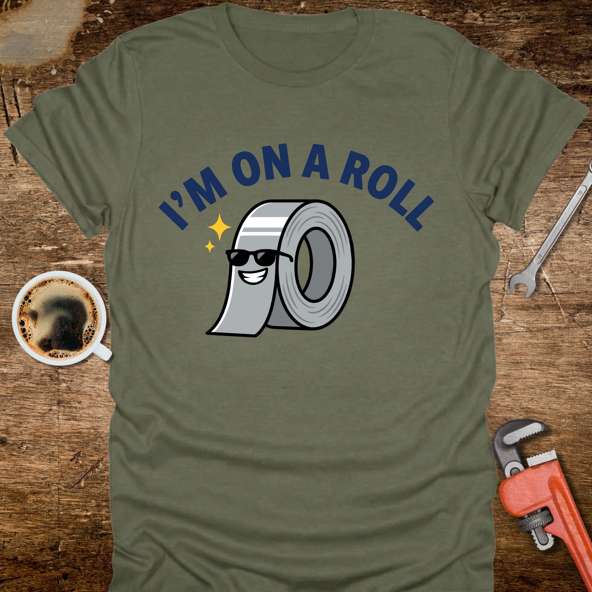 Green t-shirt with 'I'm on a Roll' graphic design on a wooden surface with coffee and tools.