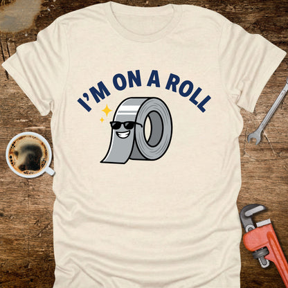 Beige t-shirt with 'I'm on a Roll' graphic design featuring duct tape, coffee cup, wrench, and pliers on a wooden surface.