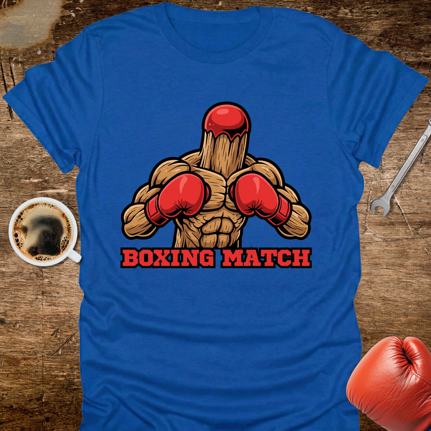 Blue t-shirt with boxing graphic and 'Boxing Match' text on a wooden surface with coffee and boxing gloves.