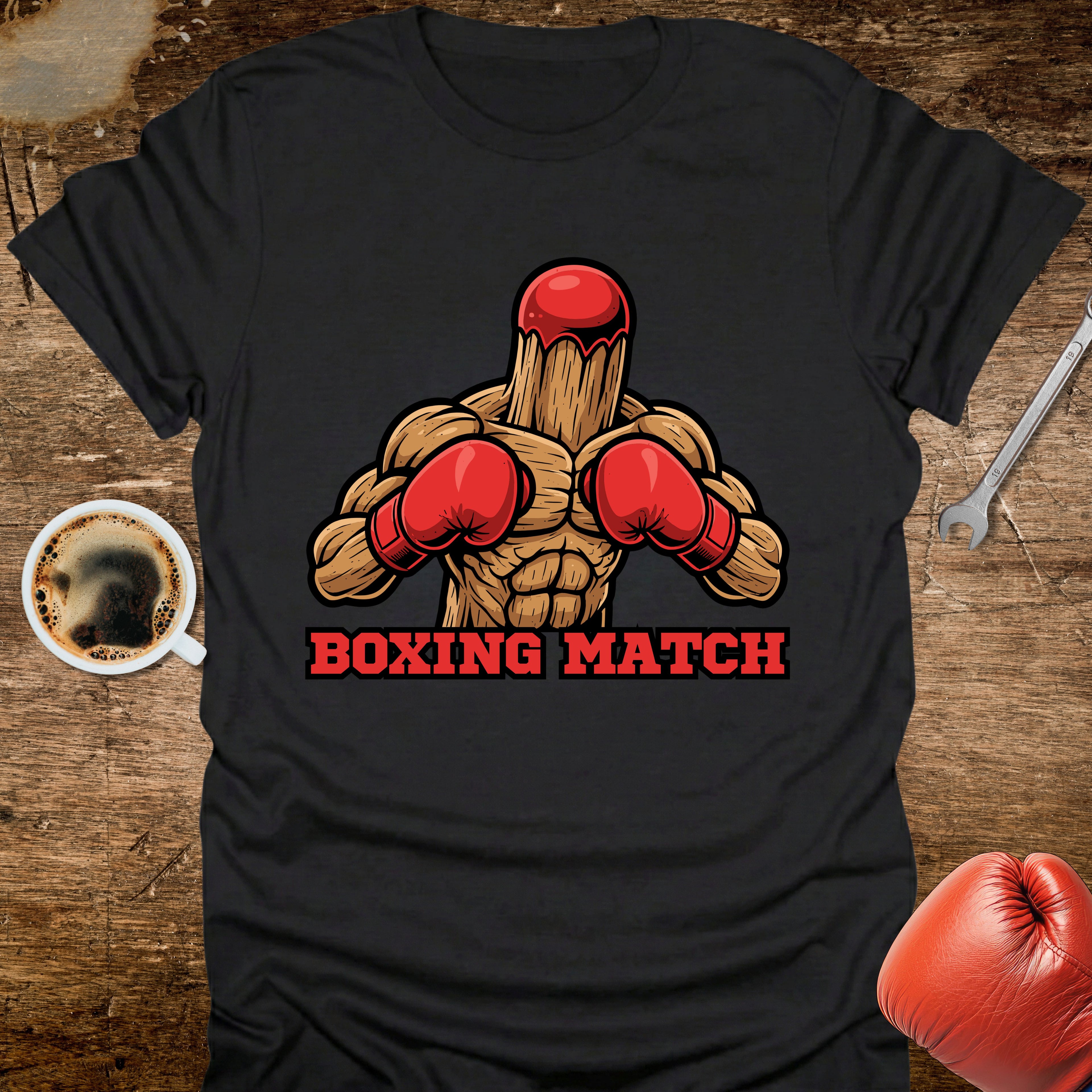 Black t-shirt with boxing-themed graphic on a wooden surface with coffee and gloves.