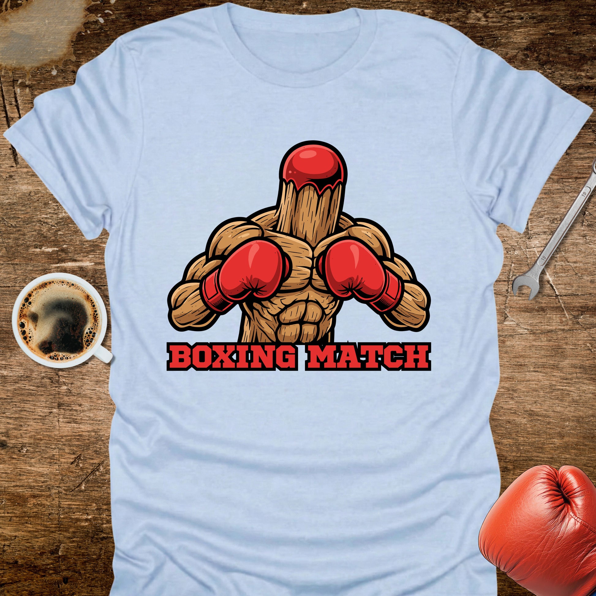 Light blue t-shirt with a boxing graphic and 'Boxing Match' text on a wooden surface with a coffee cup and boxing glove.
