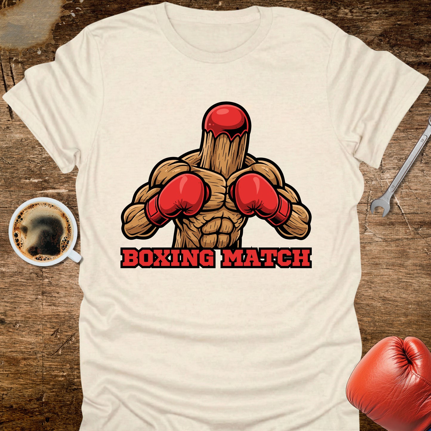 White t-shirt with boxing-themed graphic and 'Boxing Match' text on a wooden surface with coffee and gloves.