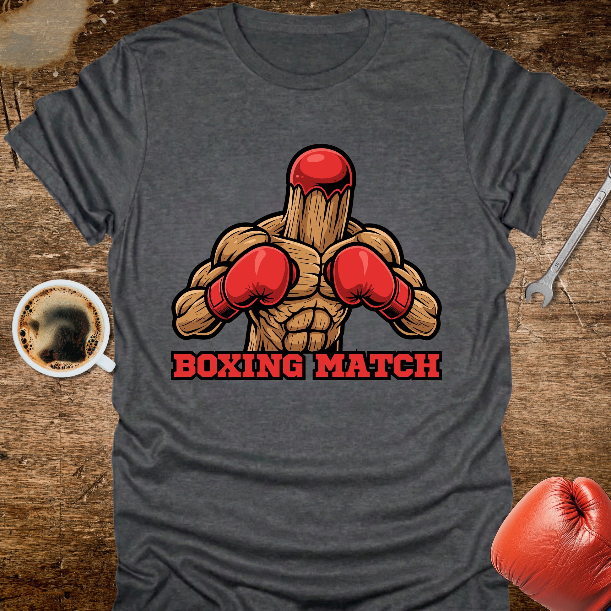 Gray t-shirt with a boxing graphic and 'Boxing Match' text on a wooden surface with coffee and boxing gloves.