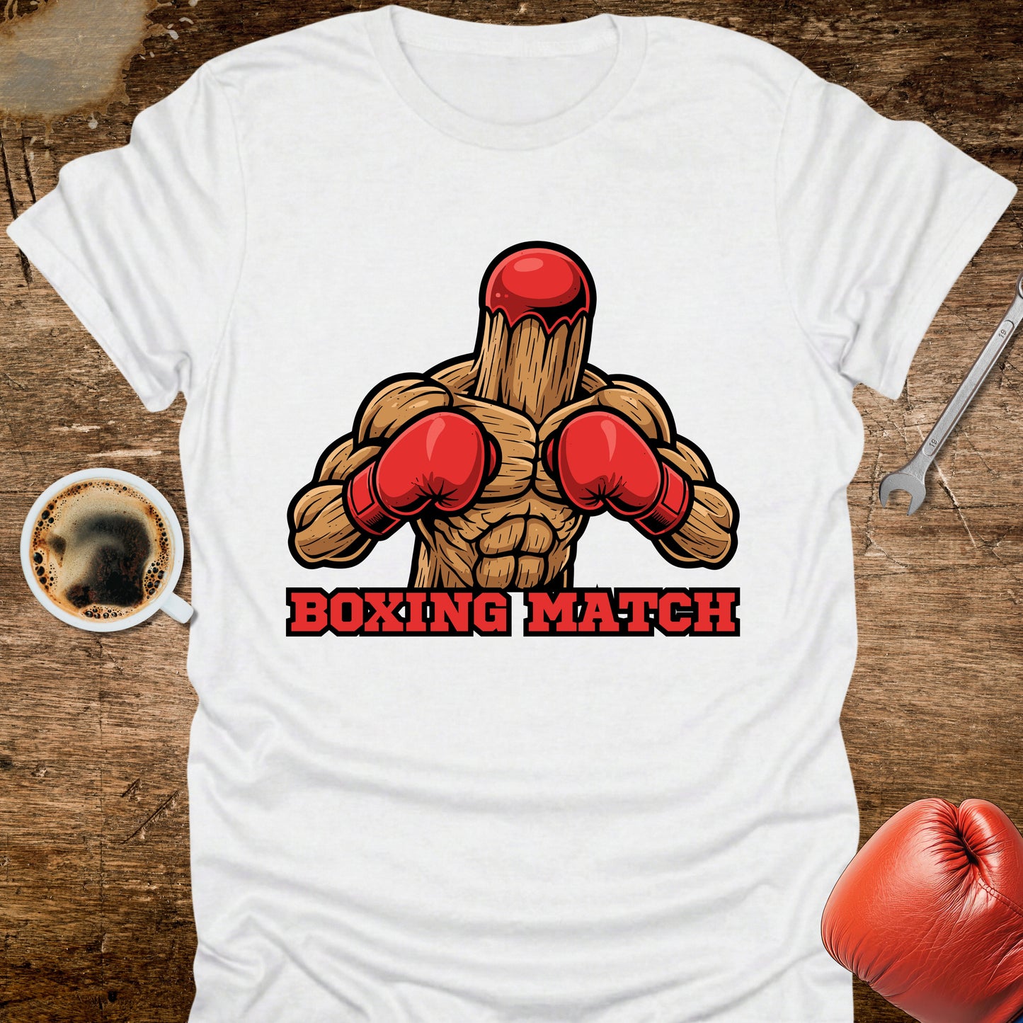 White t-shirt with boxing-themed graphic on a wooden surface with coffee and gloves.