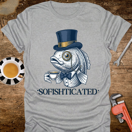 Gray t-shirt with a fish wearing a top hat and bow tie holding a cup, labeled 'Sofishticated', on a wooden surface with a cup and tools.