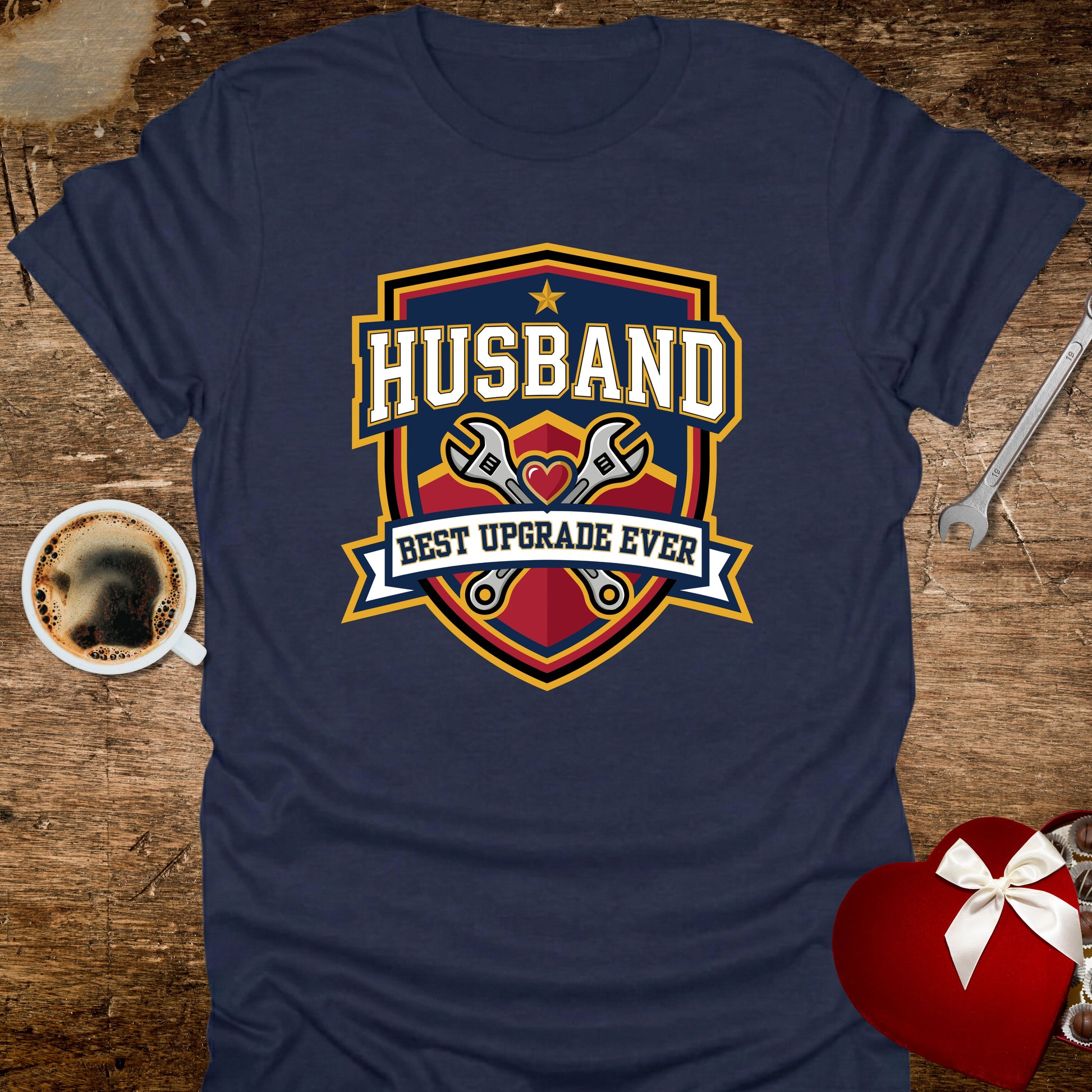 Navy blue t-shirt with 'Husband Best Upgrade Ever' graphic on a wooden surface with coffee and tools.
