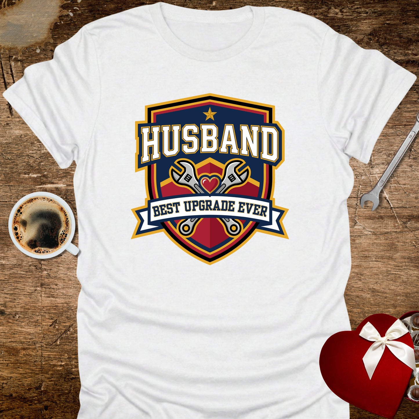 White t-shirt with 'Husband Best Upgrade Ever' graphic on a wooden surface with coffee and gift.