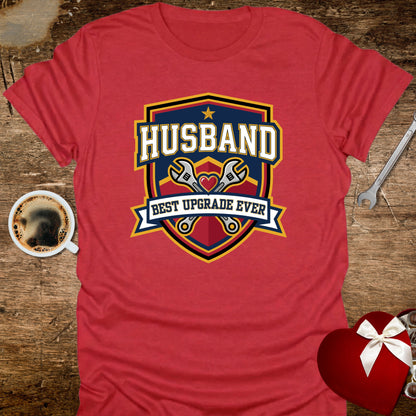 Red t-shirt with 'Husband Best Upgrade Ever' graphic on a wooden surface with coffee and tools.