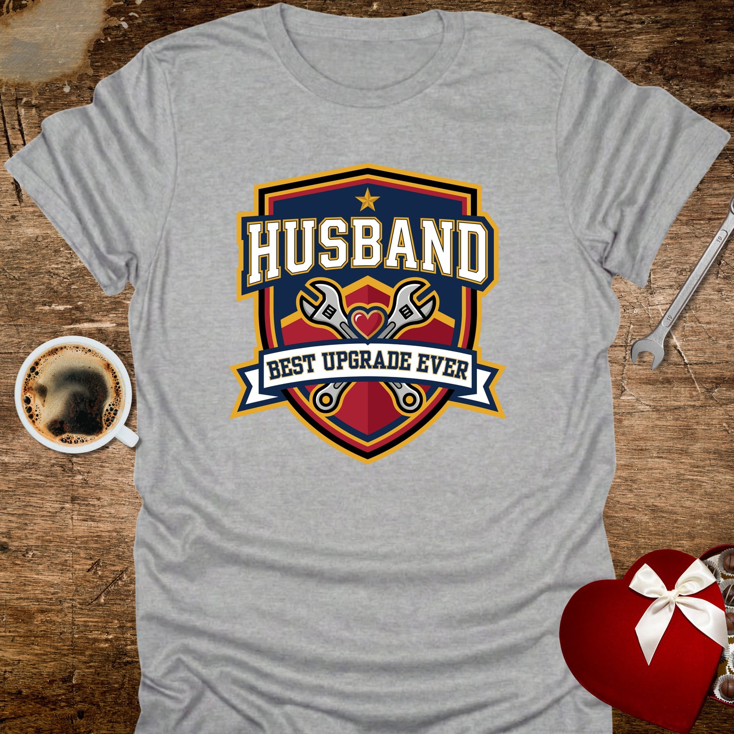 Gray t-shirt with 'Husband Best Upgrade Ever' graphic on a wooden surface with coffee and gift.
