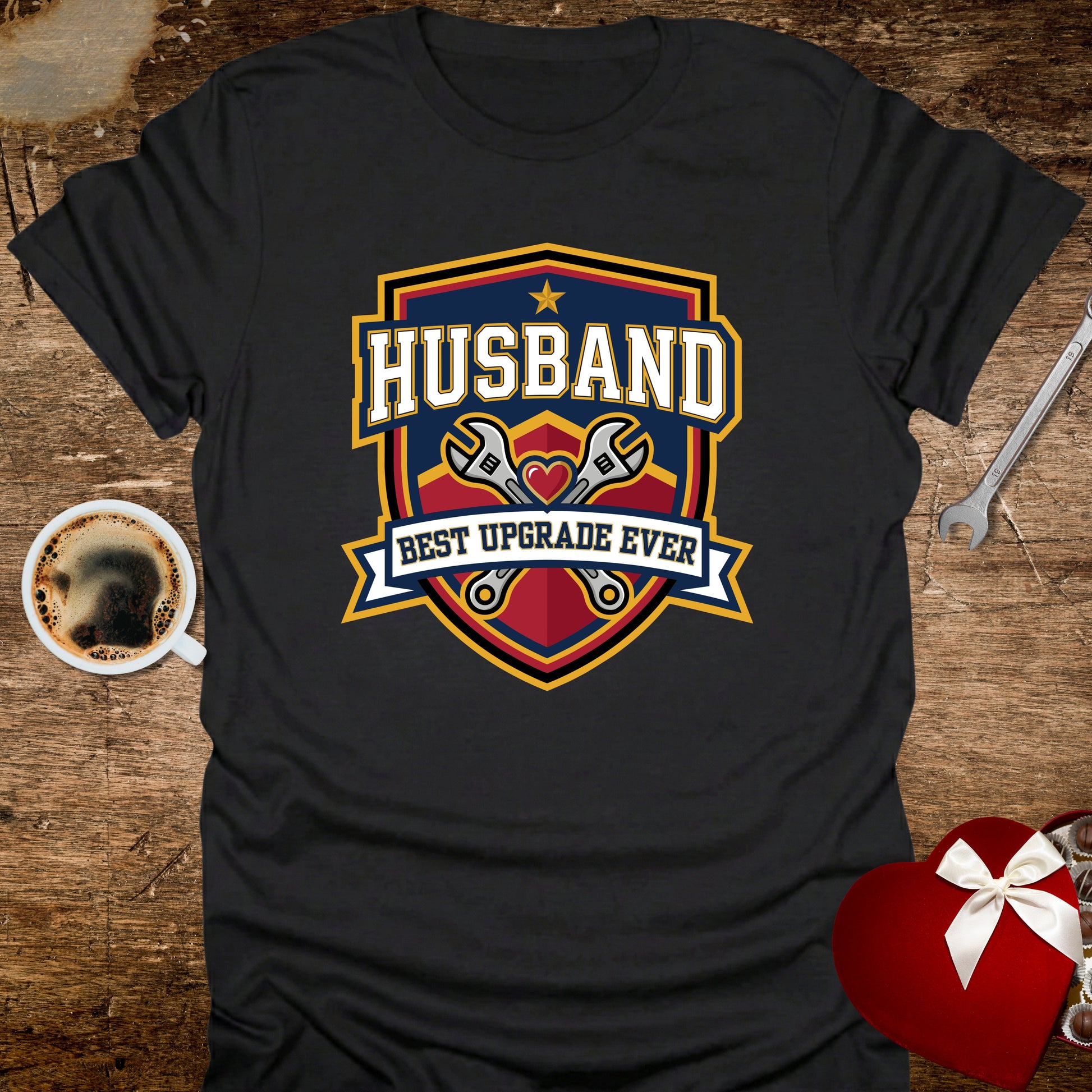 Black t-shirt with 'Husband Best Upgrade Ever' design on a wooden surface with coffee and tools.