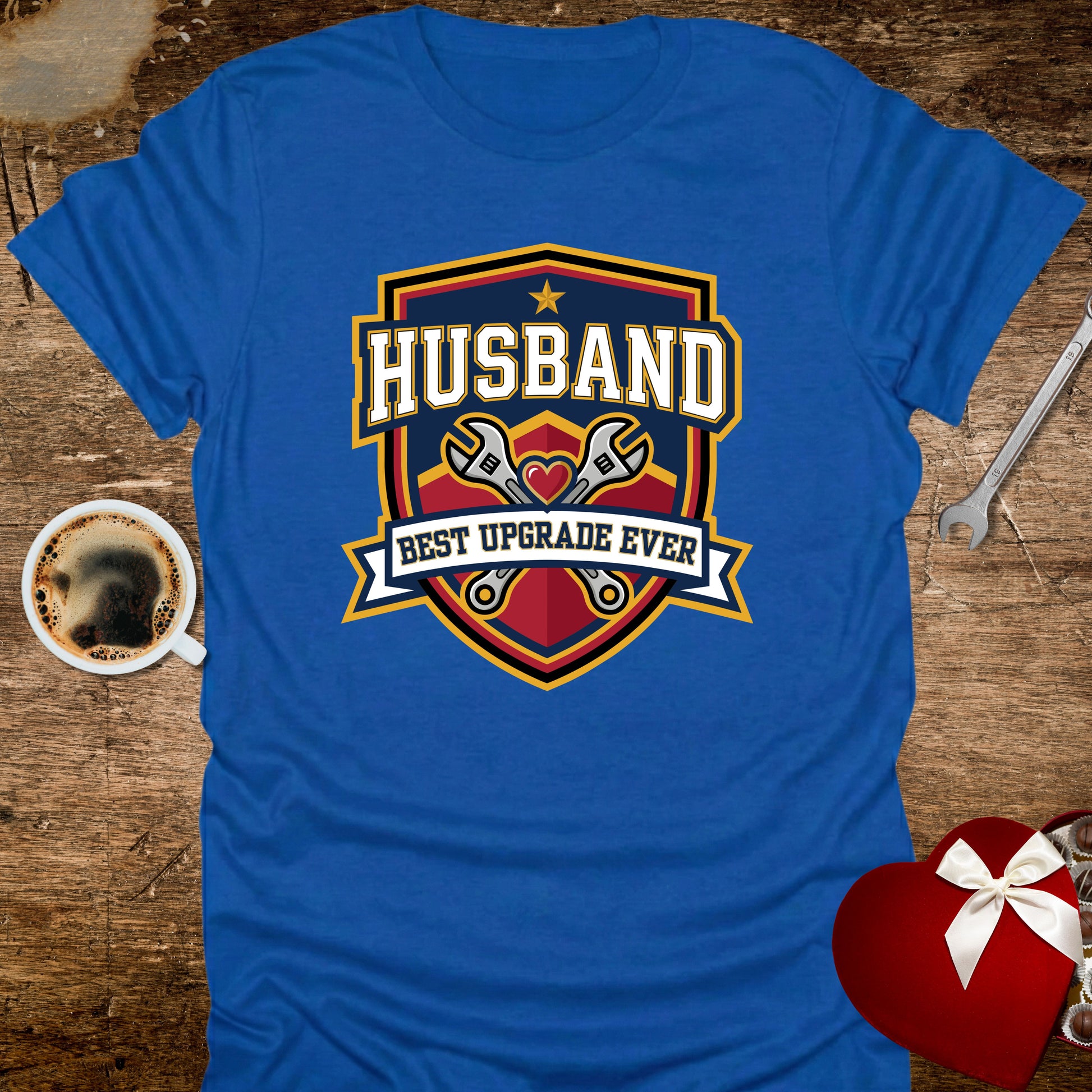 Blue t-shirt with 'Husband Best Upgrade Ever' design on a wooden surface with coffee and gift.