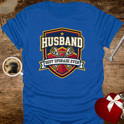Blue t-shirt with 'Husband Best Upgrade Ever' design on a wooden surface with coffee and gift.