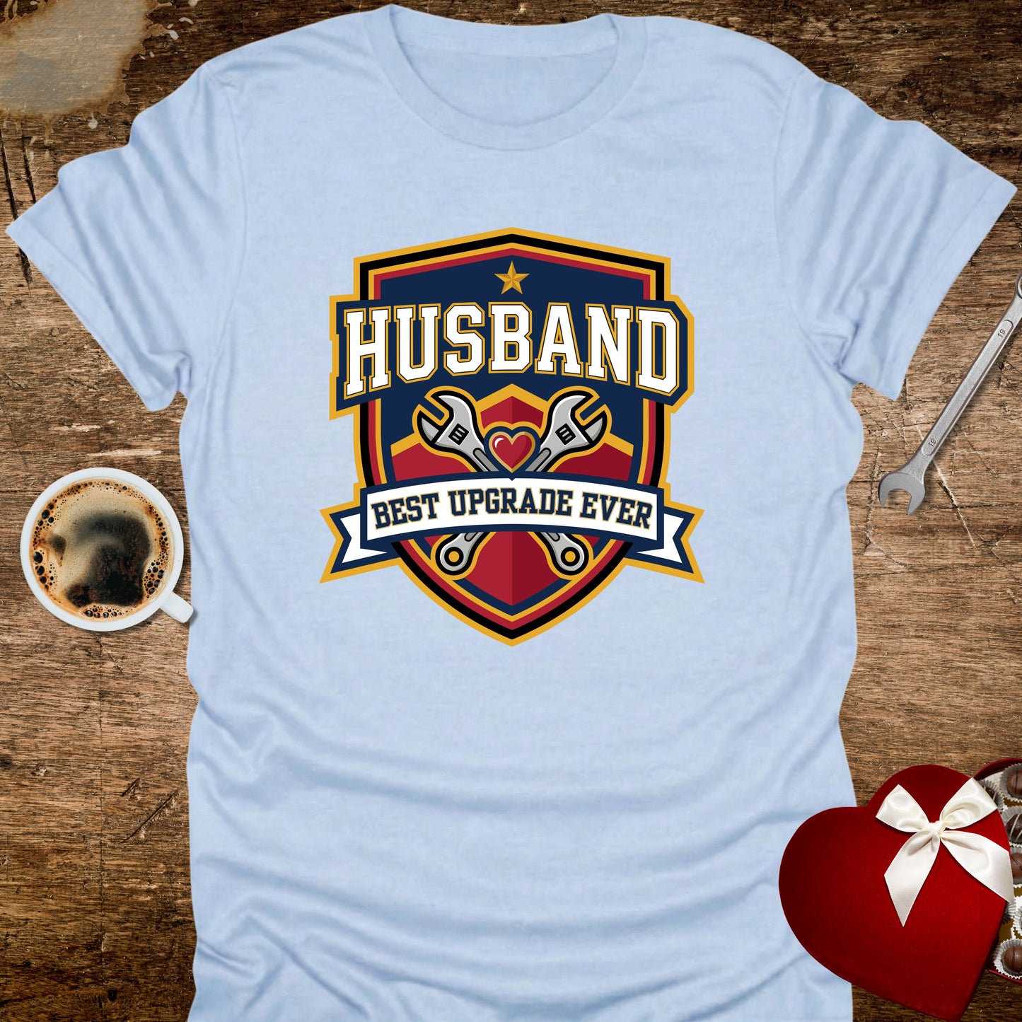 Light blue t-shirt with 'Husband Best Upgrade Ever' graphic on a wooden surface with coffee and gift.