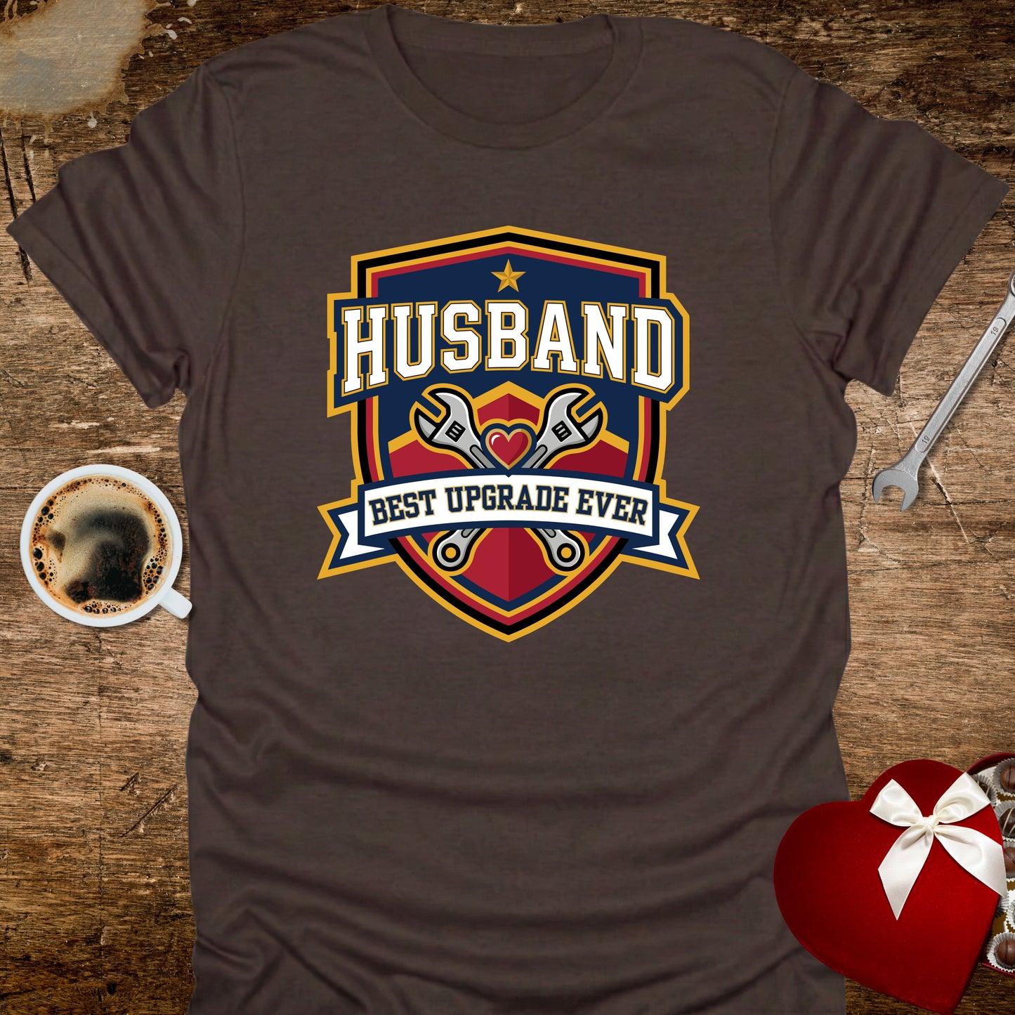 Brown t-shirt with 'Husband Best Upgrade Ever' graphic on a wooden surface with coffee and tools.