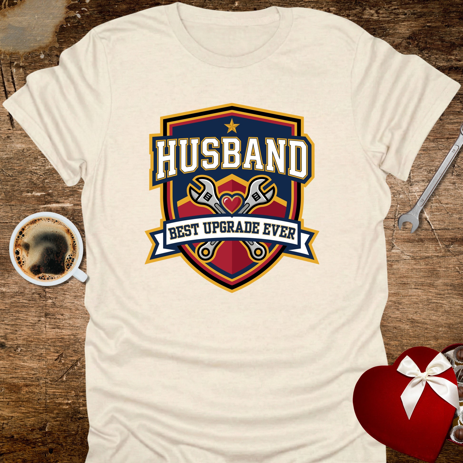 White t-shirt with 'Husband Best Upgrade Ever' graphic on a wooden surface with coffee and tools.