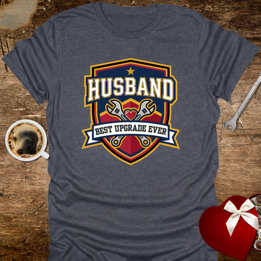 Gray t-shirt with 'Husband Best Upgrade Ever' graphic on a wooden surface with coffee and gift.