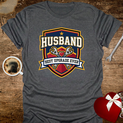 Gray t-shirt with 'Husband Best Upgrade Ever' graphic on a wooden surface with coffee and gift.