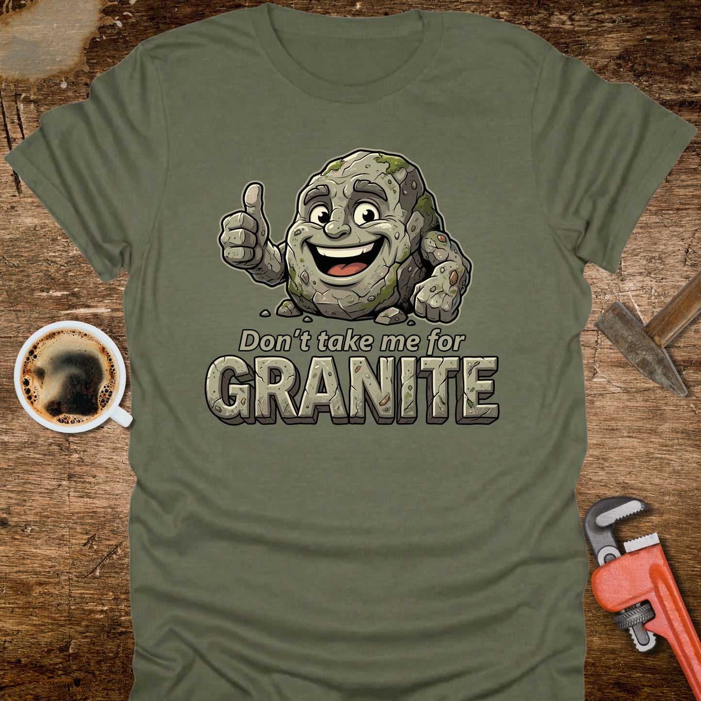 Green t-shirt with cartoon granite character and text 'Don't take me for Granite' on a wooden surface with coffee and wrench.