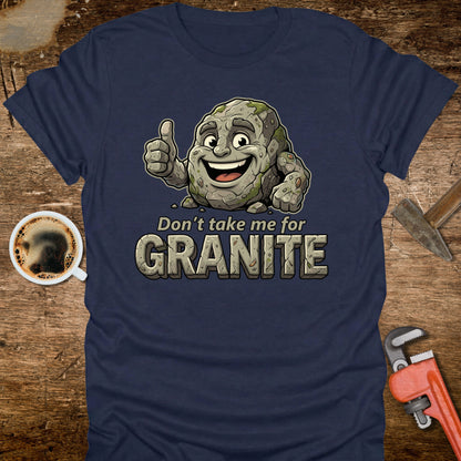 Navy blue t-shirt with a cartoon stone character and text 'Don't take me for Granite' on a wooden surface with coffee and tools.