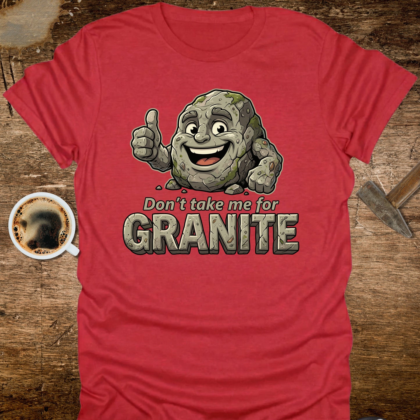 Red t-shirt with a cartoon stone character and text 'Don't take me for Granite' on a wooden surface with a coffee cup.