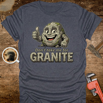Blue t-shirt with cartoon granite character and text 'Don't take me for Granite' on a wooden surface with coffee and wrench.