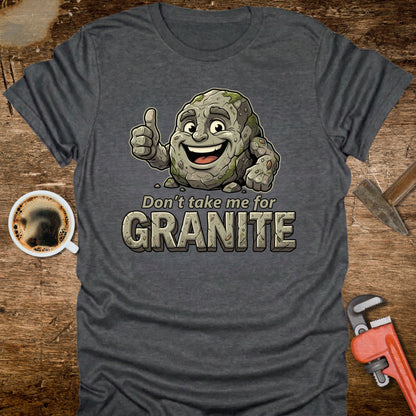 Gray t-shirt with cartoon character and 'Don't take me for Granite' text on a wooden surface with coffee and wrench.