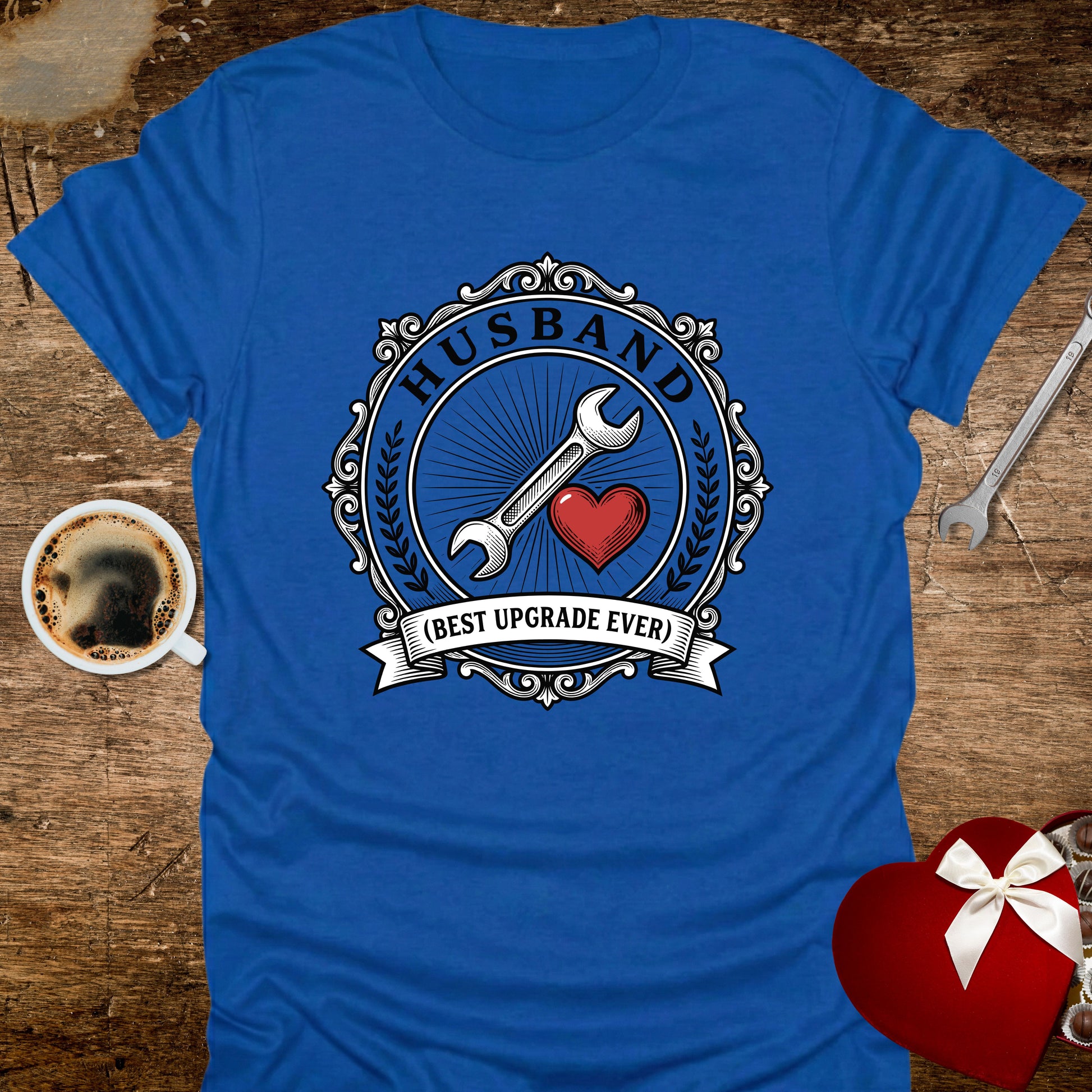 Blue t-shirt with 'Husband (Best Upgrade Ever)' design on a wooden surface with coffee and heart-shaped gift.