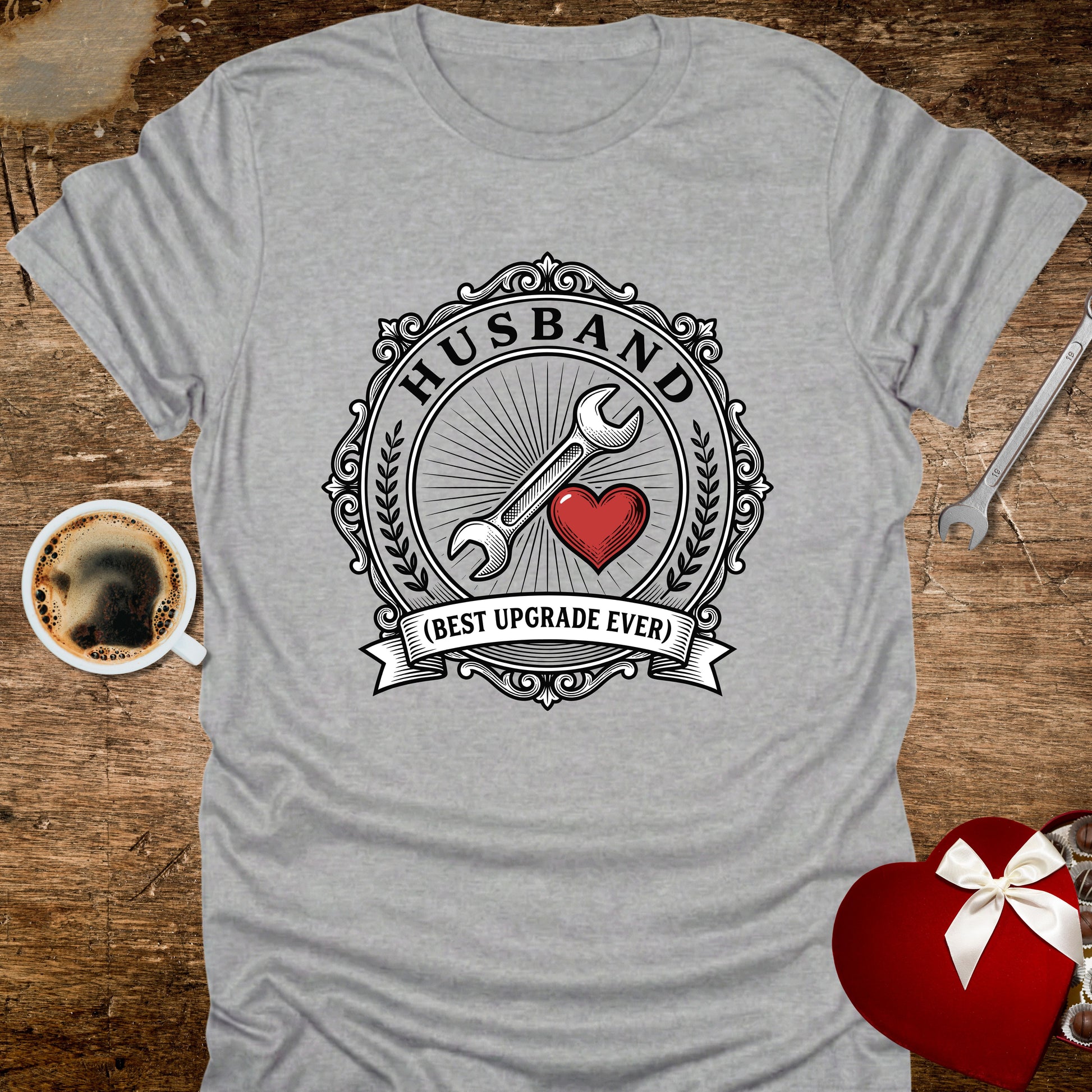 Gray t-shirt with 'Husband (Best Upgrade Ever)' design on a wooden surface with coffee and tools.