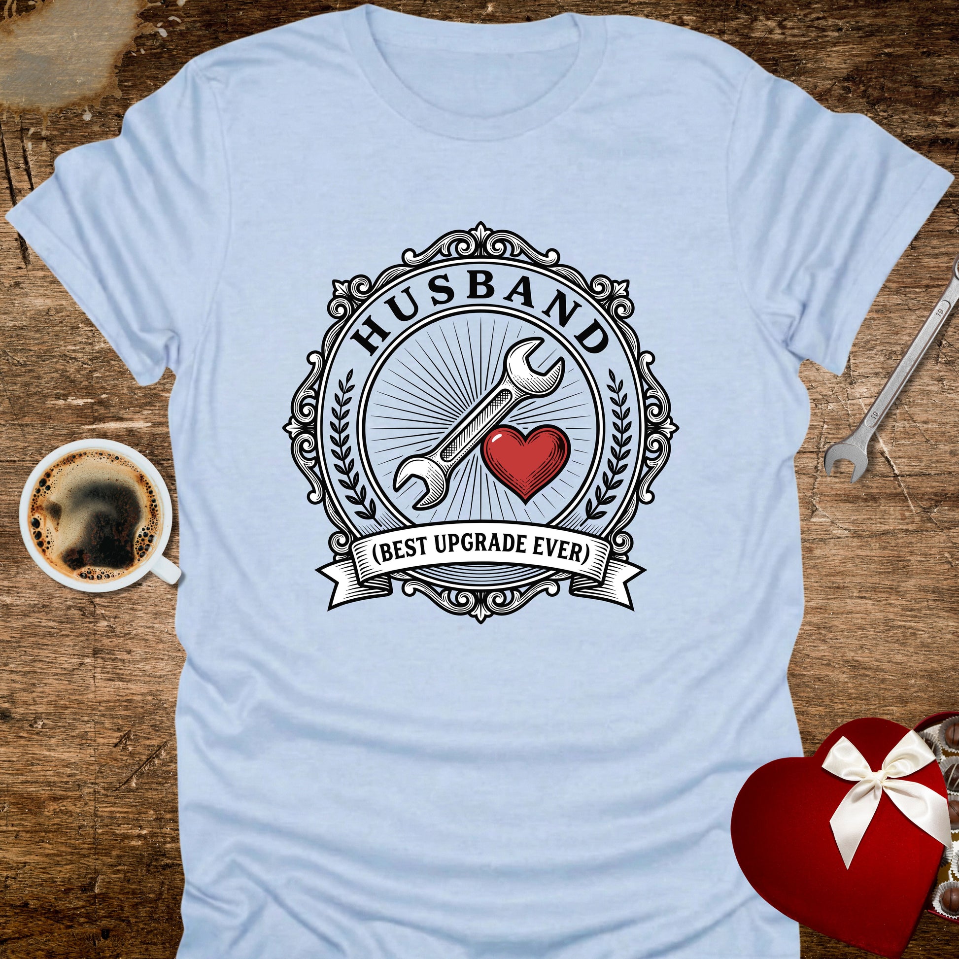 Light blue t-shirt with 'Husband (Best Upgrade Ever)' design on a wooden surface with coffee and gift.