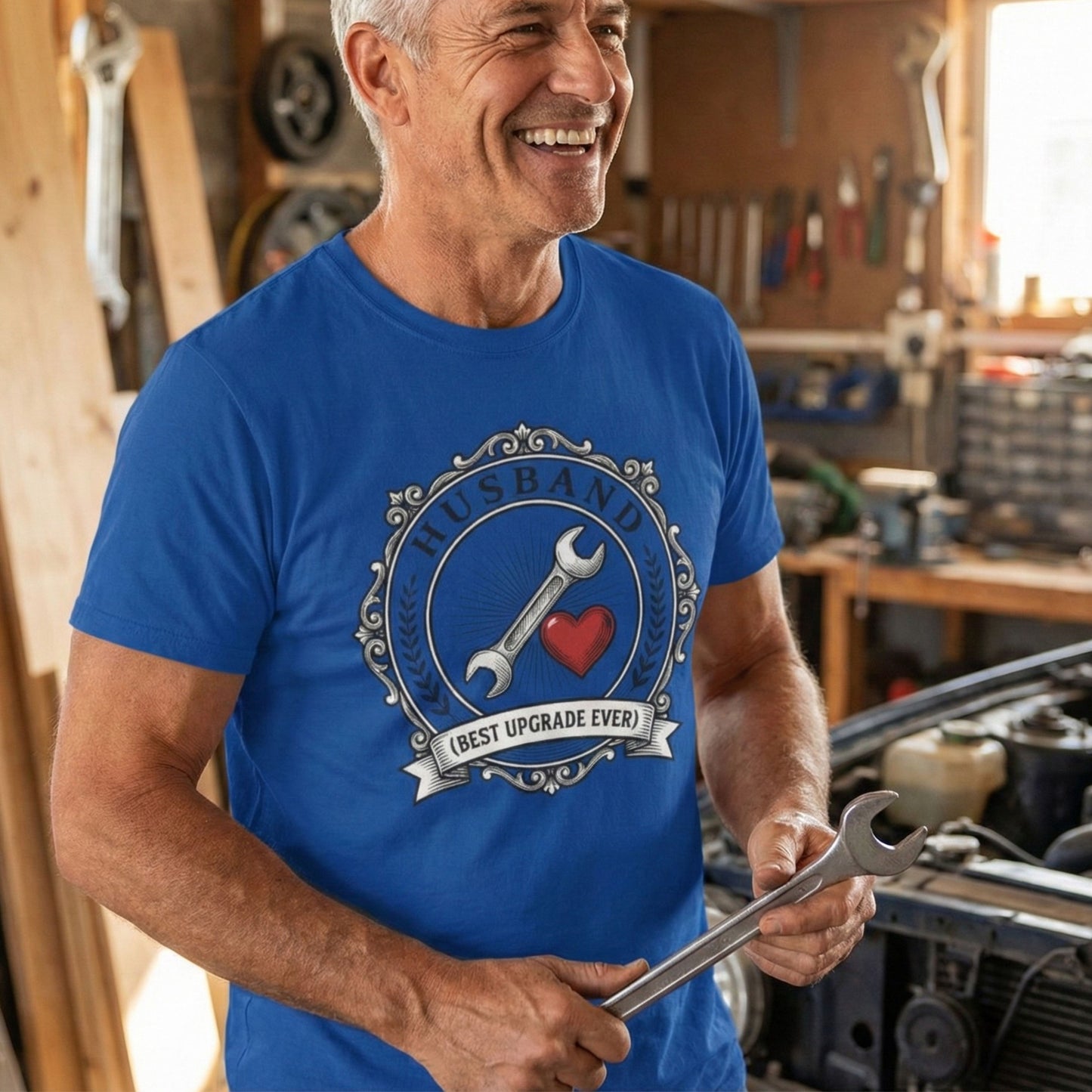 Man in a blue t-shirt with a tool graphic, holding a wrench in a workshop.