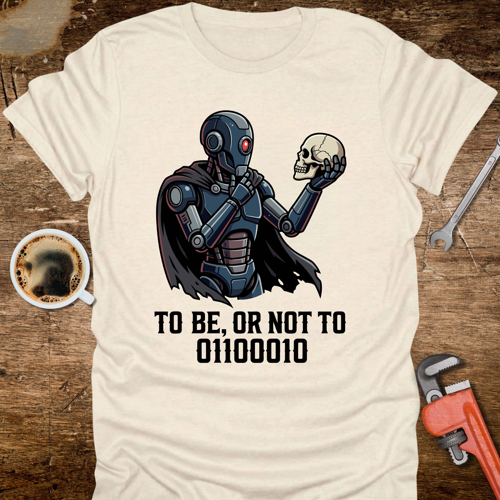 T-shirt with robot holding a skull design and text on a wooden surface with coffee and tools.