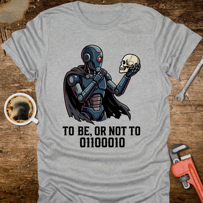 Gray t-shirt with a robot holding a skull design and text on a wooden surface with coffee and tools.