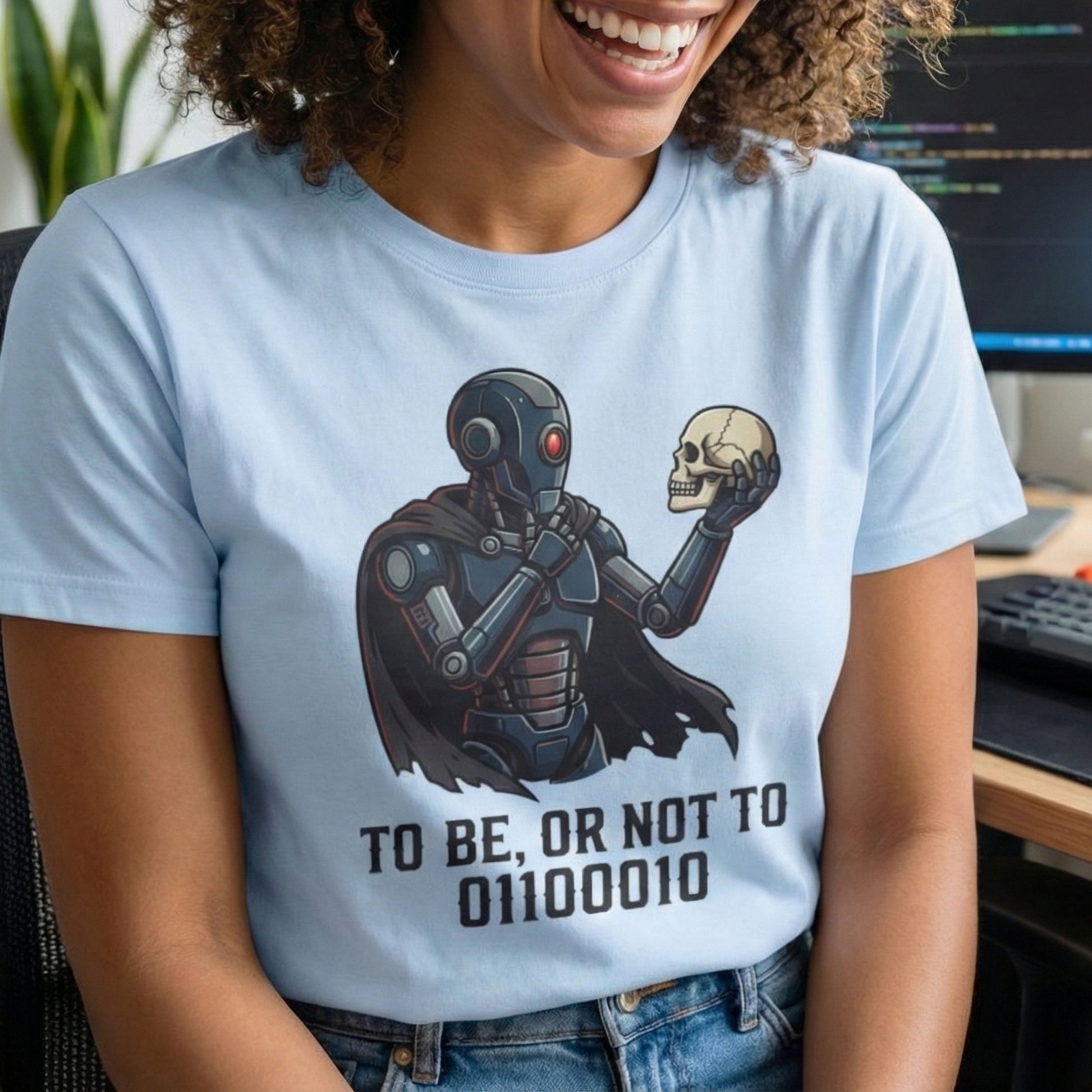 Person wearing a light blue t-shirt with a robot and skull design, sitting in an office.