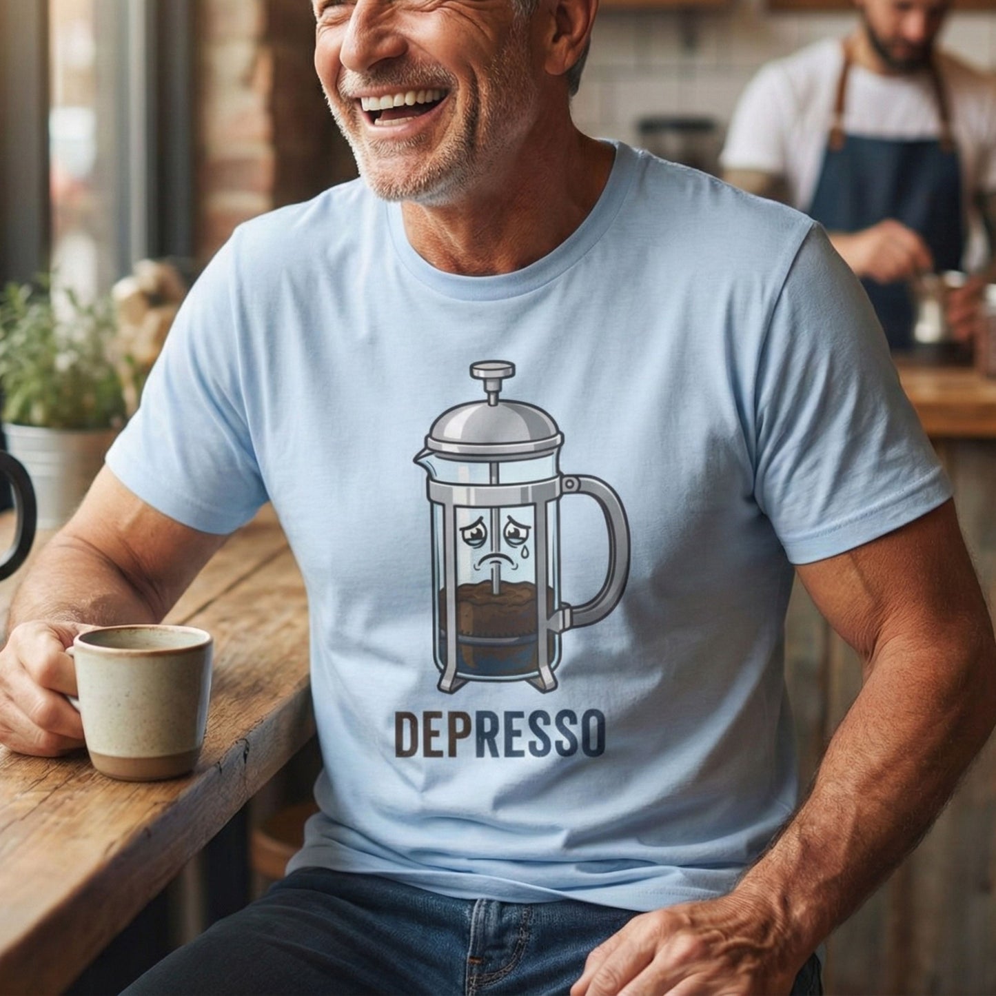 Man wearing a light blue t-shirt with a coffee-themed graphic and 'DEPRESSO' text, sitting at a table with a coffee cup.