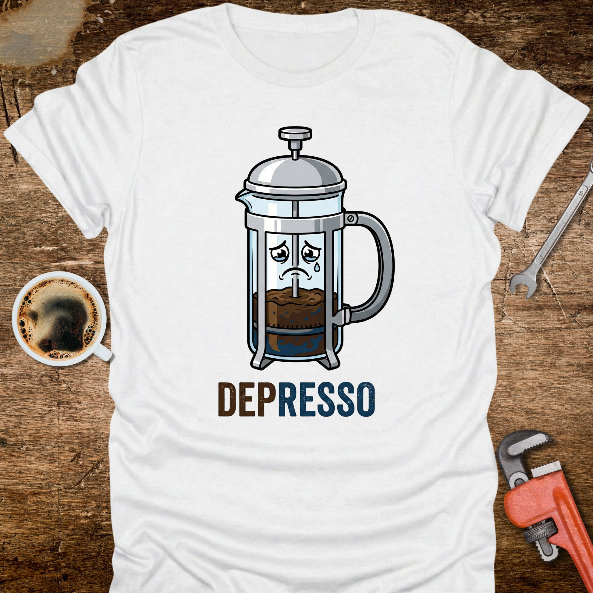 White t-shirt with a coffee-themed graphic and 'DEPRESSO' text on a wooden surface with a coffee cup and tools.