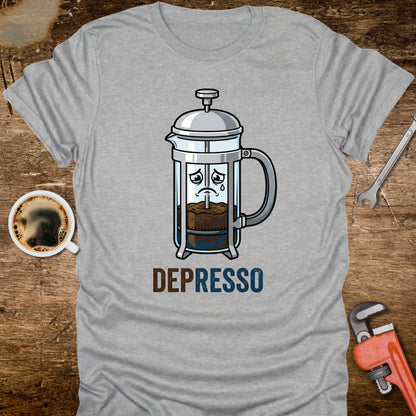 Gray t-shirt with a French press graphic and 'DEPRESSO' text on a wooden surface with coffee and tools.