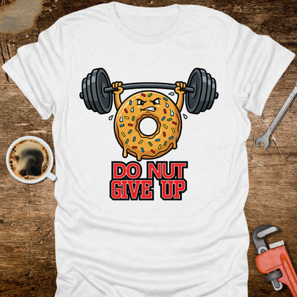 White t-shirt with a donut lifting weights graphic and 'Do Nut Give Up' text on a wooden surface.