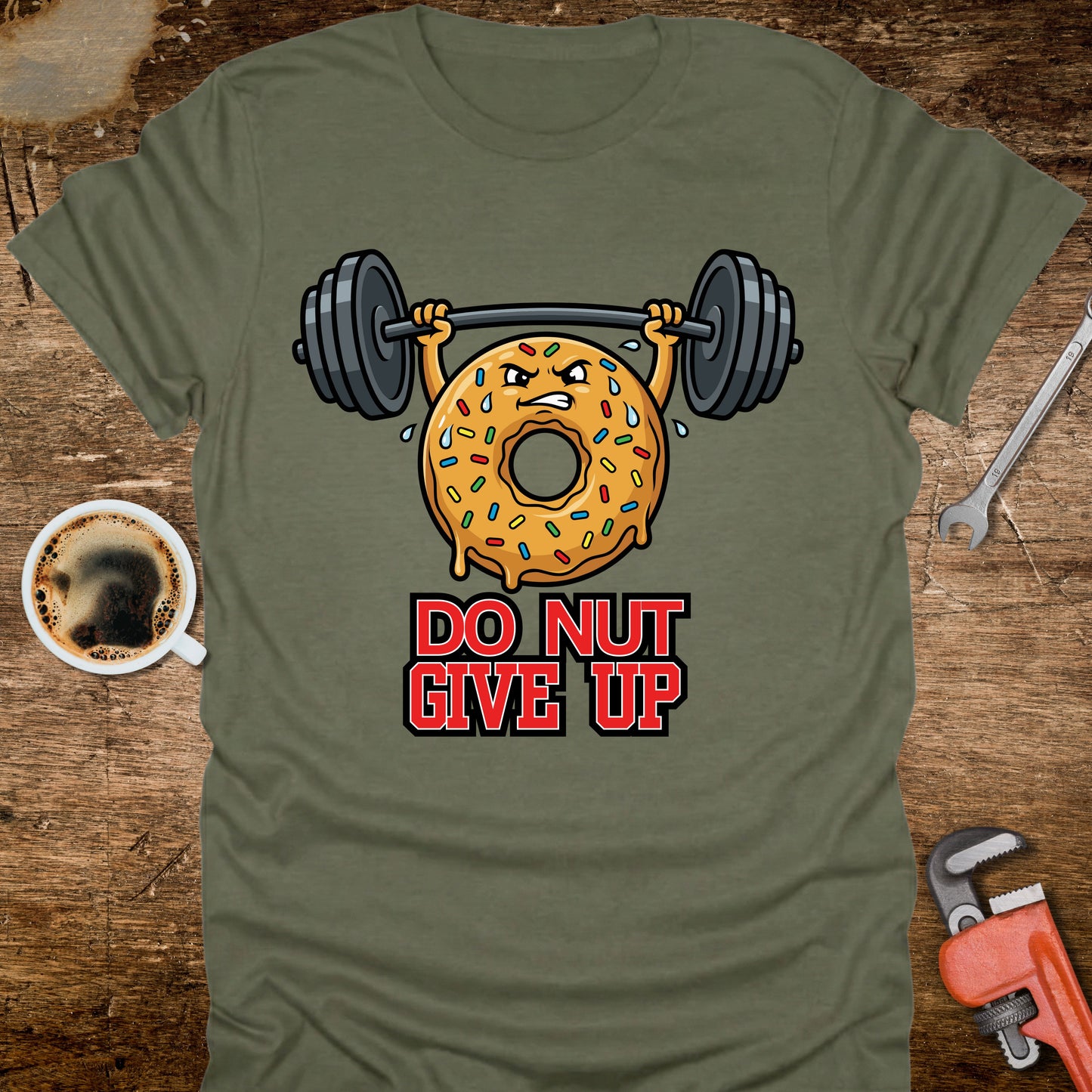 Green t-shirt with a donut lifting weights graphic and 'Do Nut Give Up' text on a wooden surface.