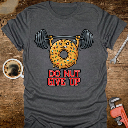 Gray t-shirt with a donut lifting weights graphic and 'Do Nut Give Up' text on a wooden surface with coffee and tools.